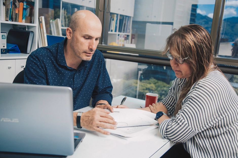Coworkers working together with documents while sitting at table with laptop near window in modern light office