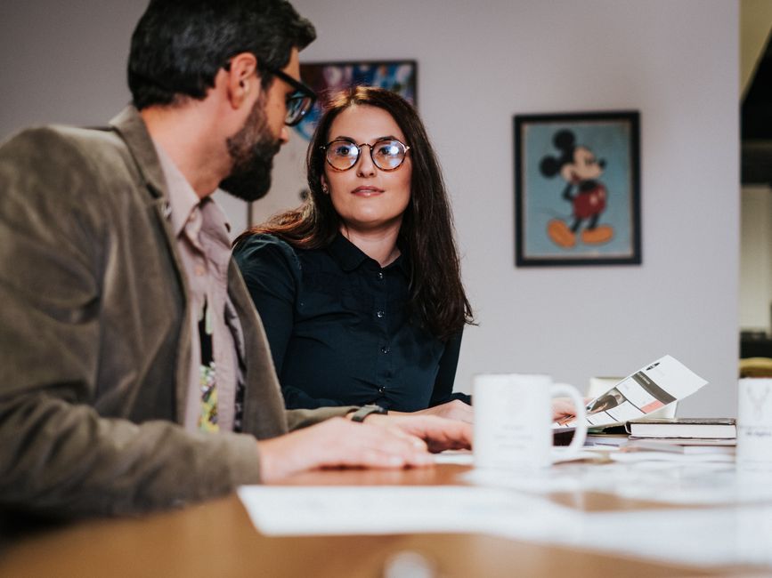 Two colleagues discussing work over coffee in a modern office setting, focusing on collaboration and teamwork.